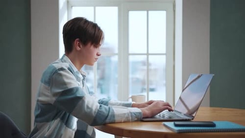 Young Adult Typing on Laptop at Table