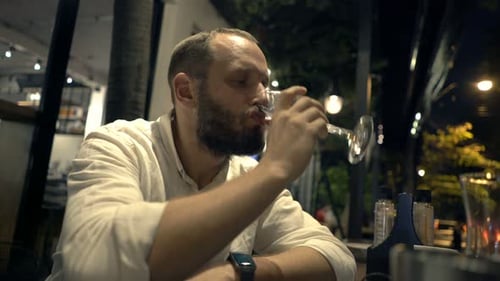Lonely young man sits alone drinking red wine in a city cafe at night