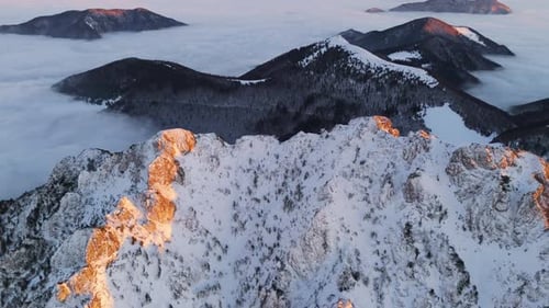 Aerial View of Snowy Rocky Peaks Illuminated By Sunset Light with Fog Draping the Valley Below