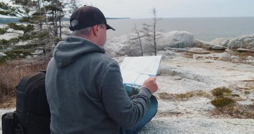 Man Studies Map on Rocky Coastal Landscape