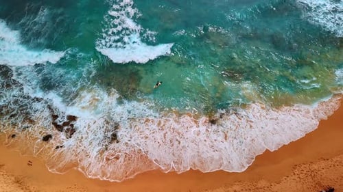Der Mann liegt auf dem Surfbrett und rudert voraus. Wellen rollen zum Sandstrand. Surfen an windigen Tagen.