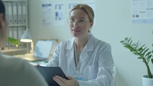 Female Doctor Reading Medical Record and Consulting Woman in Clinic
