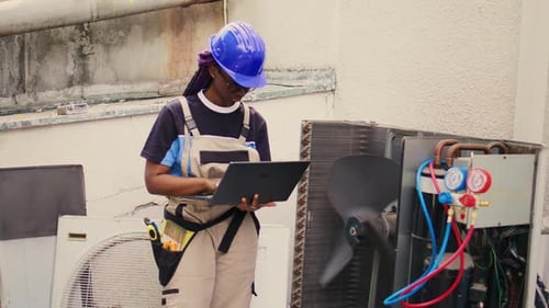 HVAC Technician Works on Laptop Next to AC Unit
