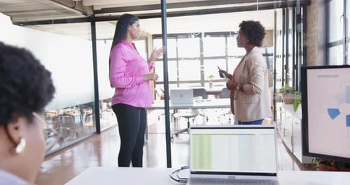 Discussing business strategy, two women standing in modern office with laptop