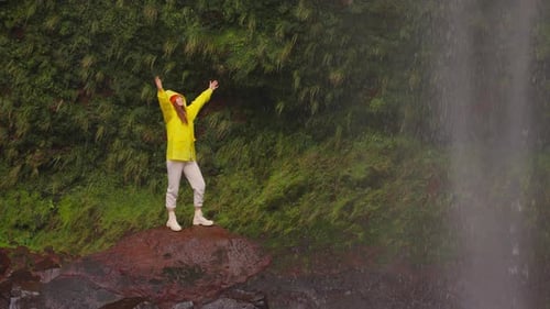 Woman Enjoying Waterfall Adventure in Yellow Raincoat