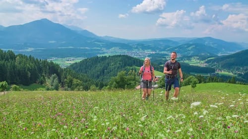 Young caucasian couple walk towards camera while hiking through alpine meadow.