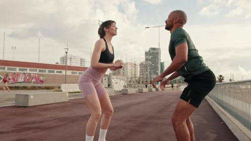 Side view of an active couple practicing outside, male and female athletes squatting