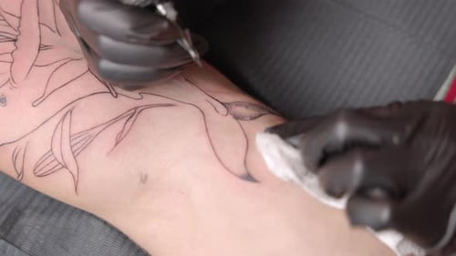 Medium shot of a tattoo artist filling in a tattoo shape on a Caucasian male's skin with black ink u