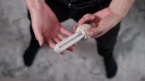 Mann inspiziert gebrauchte Kompaktleuchtstofflampe, Ansicht von oben