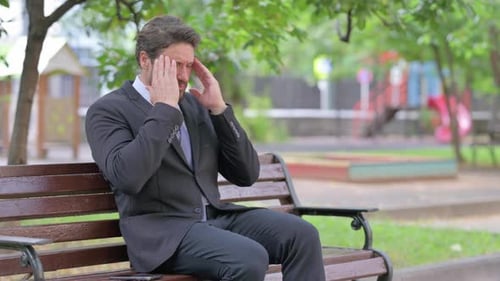 Worried Businessman Sitting on Park Bench with Headache