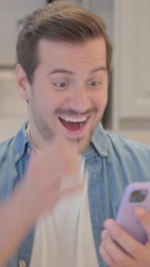 Excited Young Man Using Smartphone Indoors Celebrates Success