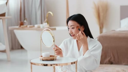 Woman Applying Makeup With Brush In Bright Bathroom