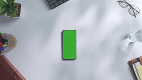 Top down view of a mock up green screen smartphone on a white office desk