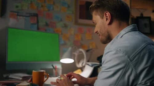 Positive freelancer typing on chromakey computer at night in his apartment