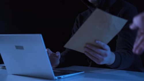 Person in Hoodie Typing on Laptop in Dark Room