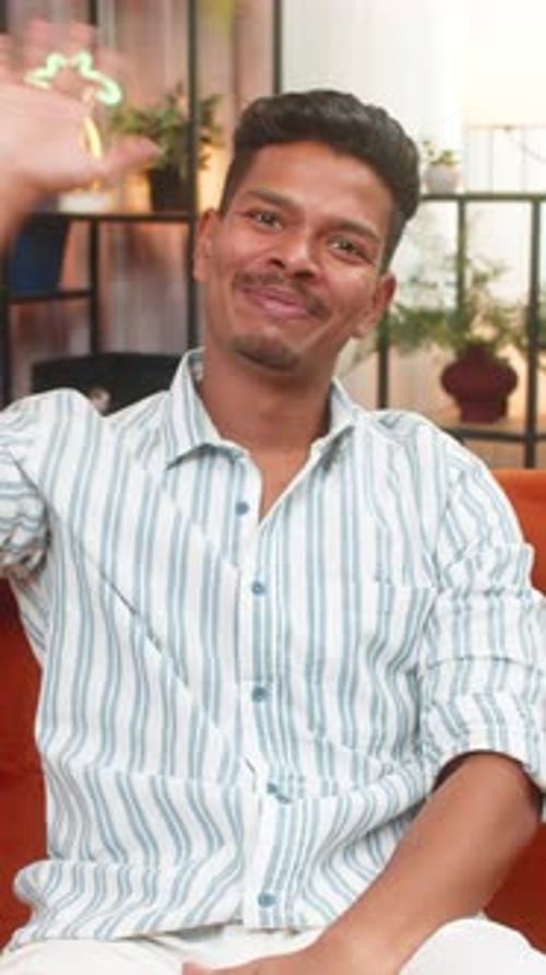Smiling young man sitting and waving hello indoors