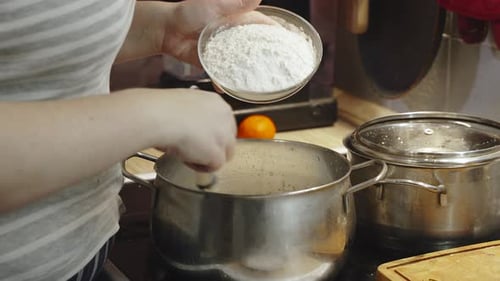 Woman Gradually Pours Flour Into Large Saucepan