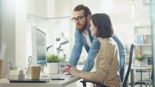 Young Man and Beautiful Woman Discuss Working Issues at Workplace. She Sits at the Table. He Stands