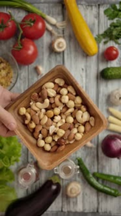 Vertical of Cook Placing Wooden Bowl of Nuts on Table with Various Ingredients