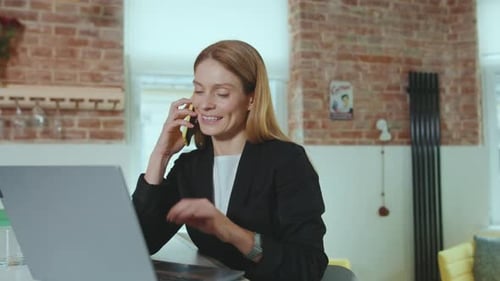 Smiling Attractive Young Businesswoman Speaking on Smartphone Use Laptop Computer at Home Office