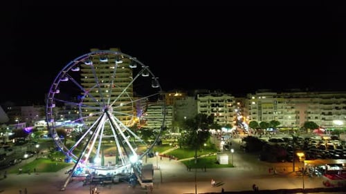 Ferris Wheel Rotates Brightly at Night in Urban Setting