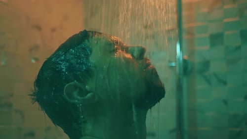 Man Standing Under Shower Water in Moody Lighting