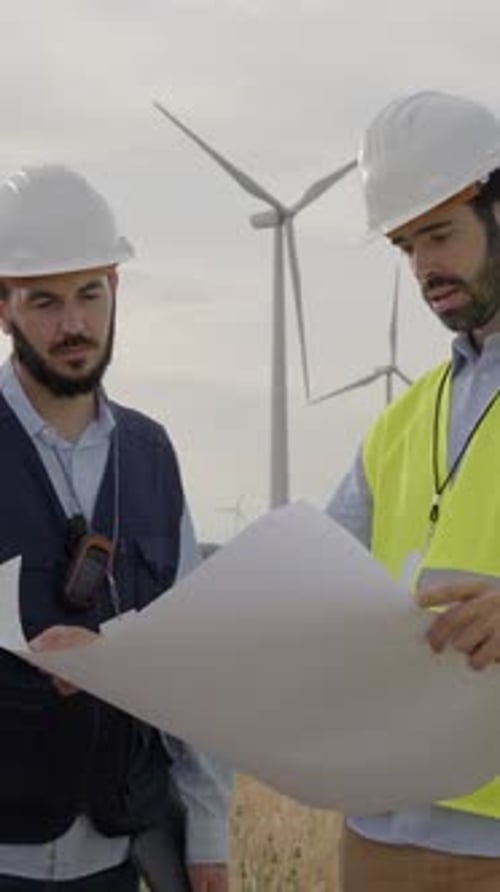 Group of Caucasian Engineers Check a Plan at an Air Turbine Field Ecology Energy and Industrial