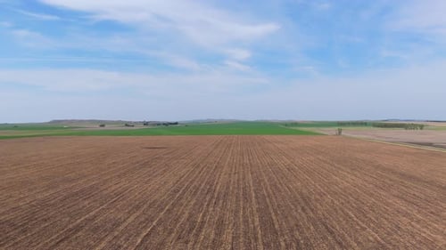 Aerial shot of a brown field, flying above, green fields in the horizon, agriculture on a sunny day