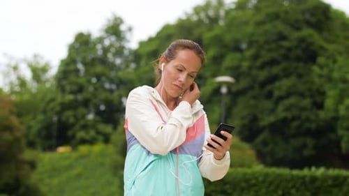 Smiling woman listens to music on smartphone and runs in park for fitness
