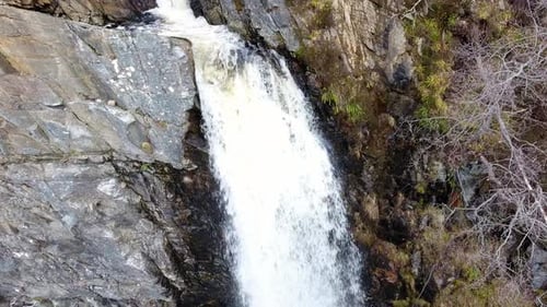 Aerial tilt down viewpoint of rocky splashing waterfall wilderness close up.