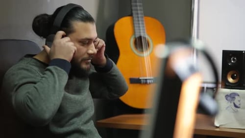 Young man wearing wireless headphones chilling listening to music sit on studio, happy relaxed guy e