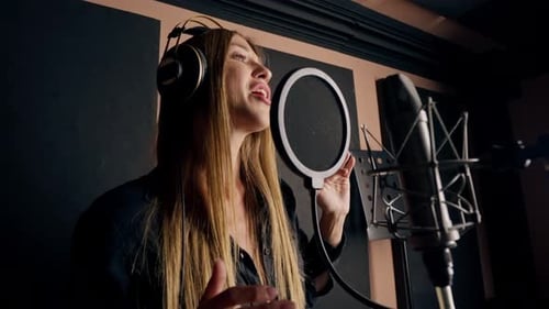 girl singer singing in a recording studio with headphones in front of microphone to create a song