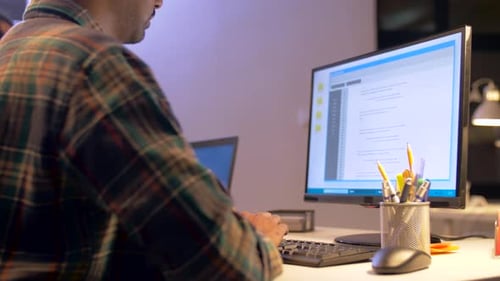 Man Types at Computer in Dark Office Setting