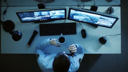 Top View of a Security Guard Looking at Monitors with Video Surveillance Footage on Them and Talkin