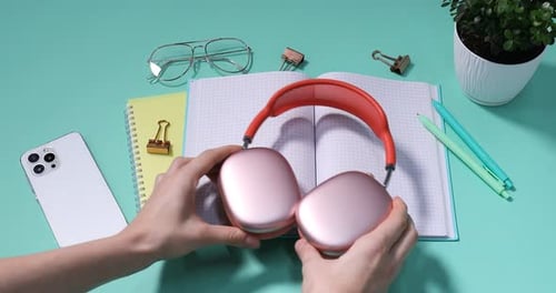 Hands placing headphones on notepad with tech accessories