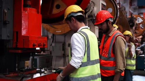 Two heavy industrial engineers check together in a steel factory.