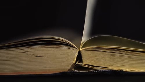 Slow motion, close up of an old, vintage, open book with pages turning on the wind, on a dark room w