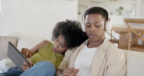 African American couple sitting on sofa she tapping tablet urging man fitting headset testing audio