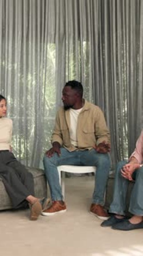 Vidéo verticale : Au milieu d'une discussion à domicile, un homme afro-américain aide une femme à se serrer chaleureusement dans ses bras pendant que son ami applaudit