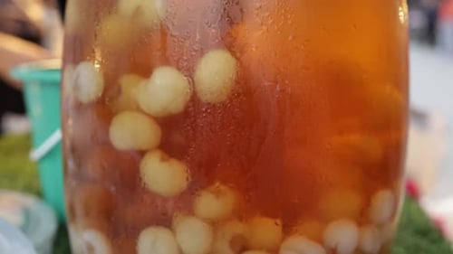 SLO MO : De la chair de longane fraîche flotte dans du jus de longane dans un grand bocal en verre sur un stand de jus de fruits au loc