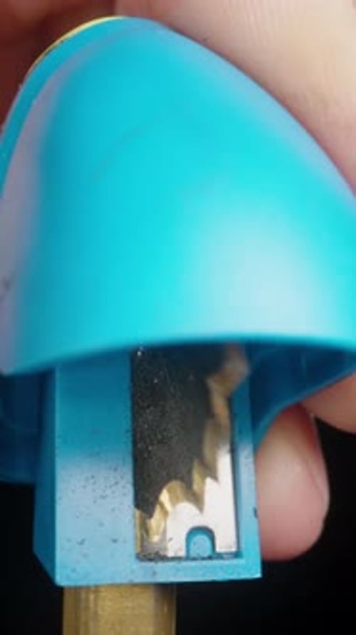 Vertical video. A man sharpens a pencil in a blue sharpener on a black background. Close-up.