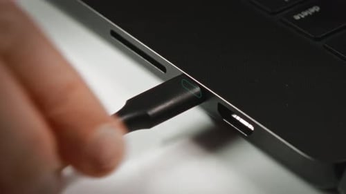 Plugging Black USB-C Cable into Laptop on Desk