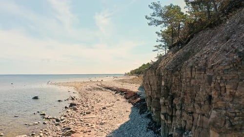 Rocky beach landscape with a cliff and pebble stone beach. Aerial establishing, camera flies past ro