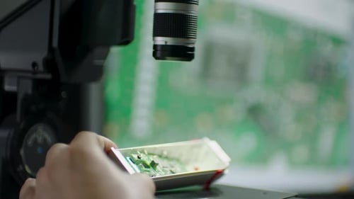 Technician Inspecting Circuit Board Under Microscope in Electronics Laboratory