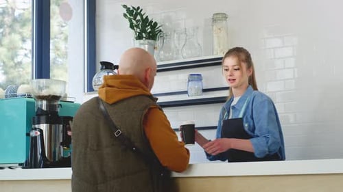 A Barista Gives Coffee to an Old Man in the Cafeteria Senior Pays Using NFC Smartphone Contactless