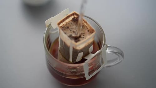 Pouring Water Into Drip Coffee Bag in Glass Mug