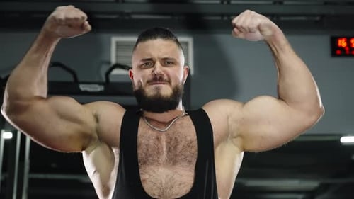 Closeup of a Muscular Bearded Athlete Doing an Intense Shoulder Workout with Arms Extended in a Lit