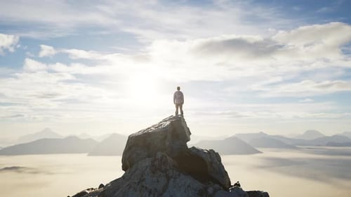 Adventurous Male Hiker Standing on Dramatic Rocky Peak. Low Clouds and Mountain Landscape. Sunny Day