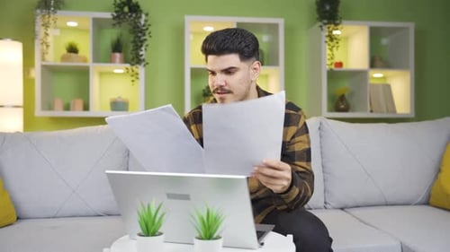 Young Adult Reviews Documents at Home on Laptop