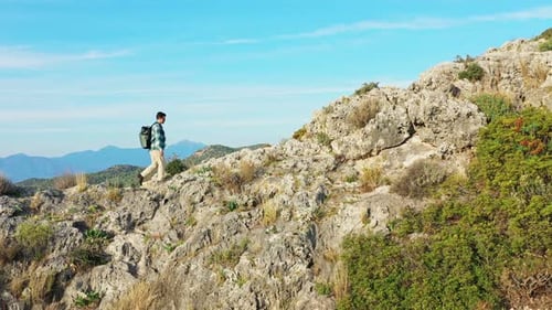 Young Man Hiking Along Rocky Mountain Top with Backpack Against Sky
